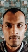 A focused portrait of a young man with a mosaic wall background, exuding seriousness.